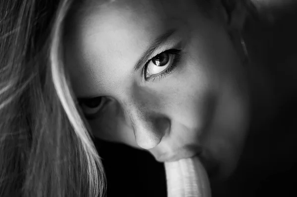 Mulher com olhar penetrante come uma banana, insinuando sexo oral.