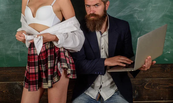 Homem de barba ao lado de uma mulher usando uniforme de estudante, em um cenário escolar sensual.
